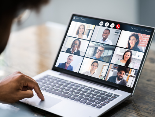 A man looks at a computer screen that has numerous people smiling and talking online as a group.