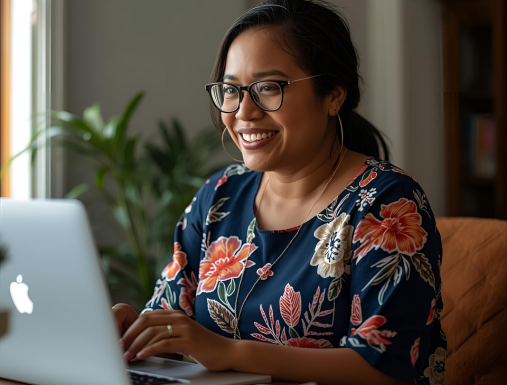 A woman with glasses on and earbuds talks smiles as she stares at computer as part of training.