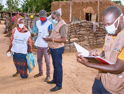 A group of people with notebooks walk around a rural village in Niger.