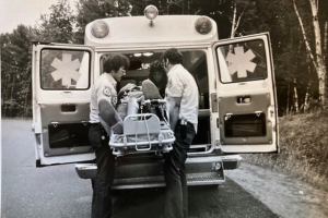Old black and white photo of a person being placed in an ambulance while on a stretcher