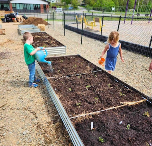 Two small children tending to a freshly plowed raised garden bed outside.