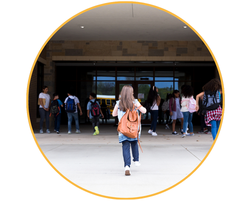Back of young girl running into a school building with a backpack on