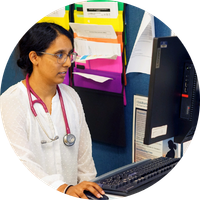Female doctor wearing glasses and white coat looks at her computer screen while in her office.