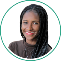 Woman with braided hair smiling at camera in brown shirt.