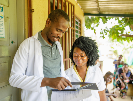 A man and a woman look over a book outside a health facility.