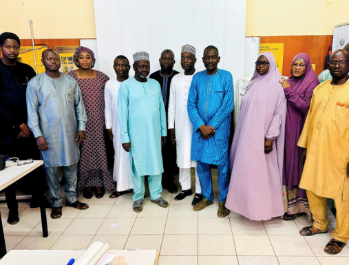 A group of people pose for a camera in different colored clothing after completing a training in Uganda.