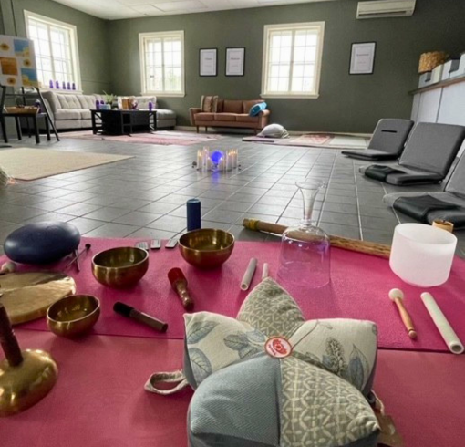 Image of a blanket with pillows on a floor in a big room with sound bath instruments
