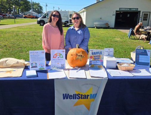 Two people smiling behind a table outside in Maine with WellStarME resources on it.