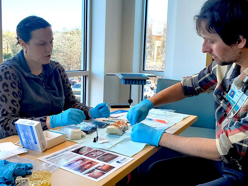 Two people in training with blue gloves over oral health items.