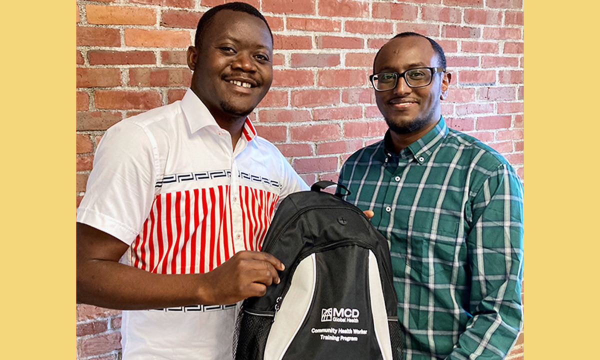 Two men posing for the camera holding a MCD CHW backpack as part of MCD's CHW training program.