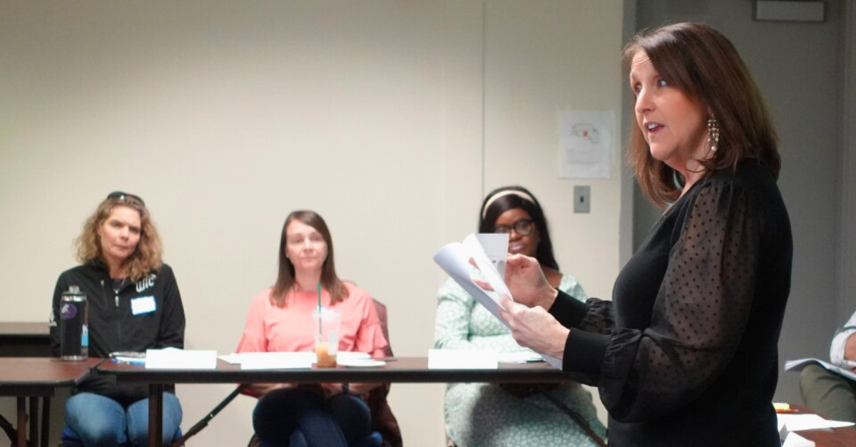 A woman standing up and talking to a room filled with people