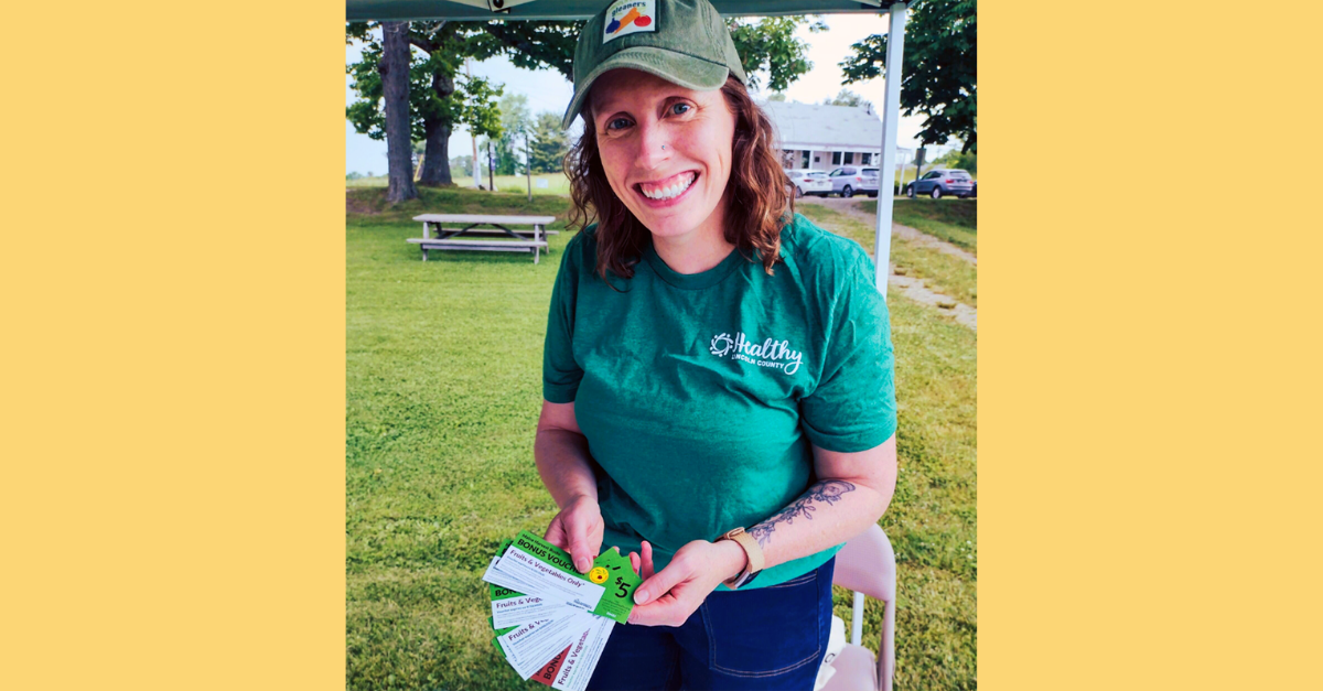 A smiling woman wearing a hat holding out $5 voucher tickets.