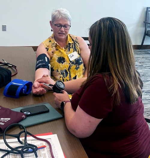 Two people sitting at a table with one wearing a blood pressure cuff and the other taking measurements.