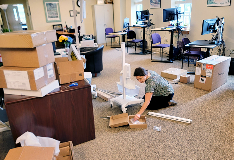 Danielle Louder sits on the floor as she starts to put together the delivered telehealth equipment in an office setting.