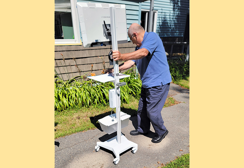 Man rolls a newly set-up telehealth kiosk wiht monitor and other technology into a PNMI site.