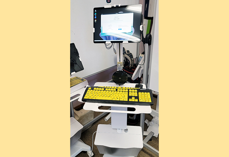 Tablet hooked onto mobile cart with keyboard, mouse and headphones used for telehealth appointments.