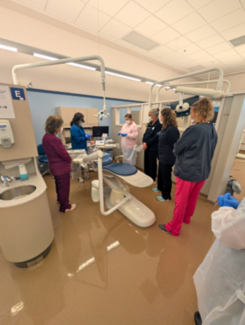Photo of dental hygienists aruond a dental chair room with a woman leading the course.