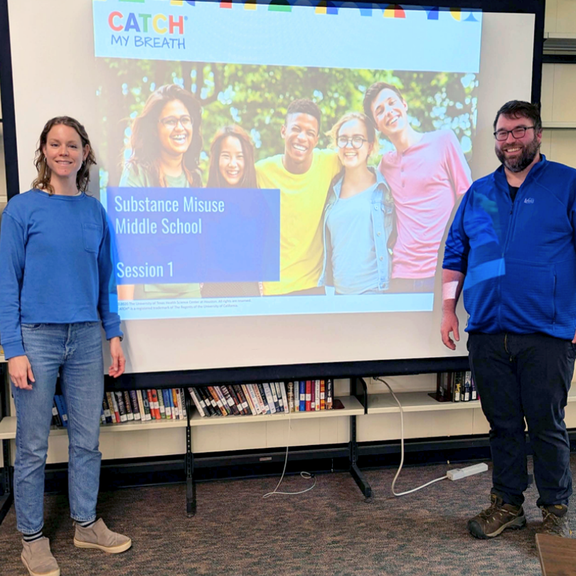 A young man and woman standing in front of a presentation in a classroom.