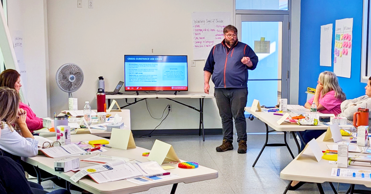 A young man standing in front of a classroom with some people in it giving a presentation